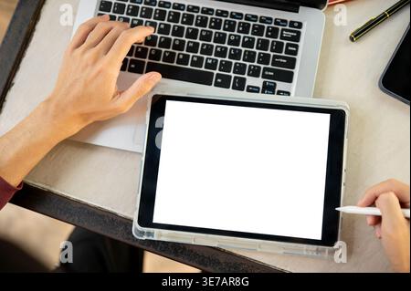 Zugeschnittenes Bild eines Thai-Mannes, der an einem Tablet und Laptop arbeitet, während er draußen am Tisch sitzt Stockfoto
