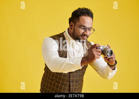 Lächelnder asiatischer Mann mit Brille, der Fotos macht, die vor gelbem Hintergrund im Studio stehen Stockfoto