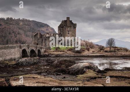 Das Eilean Donan Castle und die Bogenbrücke stehen majestätisch vor dem Hintergrund der zerklüfteten schottischen Highlands und stimmungsvoller Wolken Stockfoto