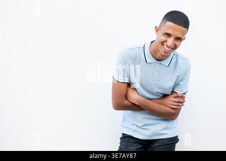 Lächelnder arabischer männlicher Teenager, der sich nach vorne lehnt und mit gekreuzten Armen vor weißem Hintergrund steht Stockfoto