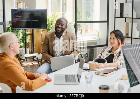 Lächelnde, verschiedene Programmierer, die sich im Büro gegenseitig zueinander treffen Stockfoto