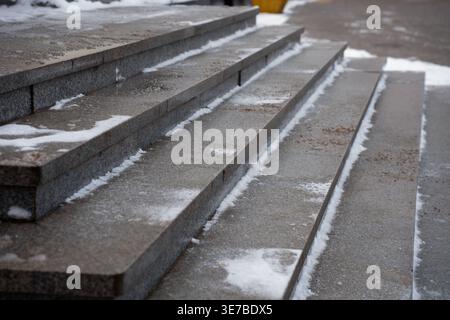 Aus nächster Nähe schräge Ansicht von feuchten Granitstufen, die leicht mit schmelzendem Schnee und Sandsand bestäubt sind, in einer urbanen Winterszene kühle Grautöne, starke führende Linie Stockfoto