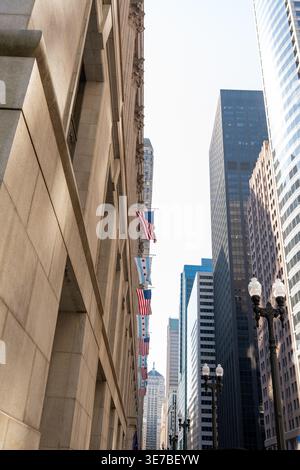 Vertikale Aufnahme einer Chicagoer Straße mit den US- und Chicago-Flaggen, die stolz neben hohen Wolkenkratzern unter einem klaren blauen Himmel zu sehen sind Stockfoto