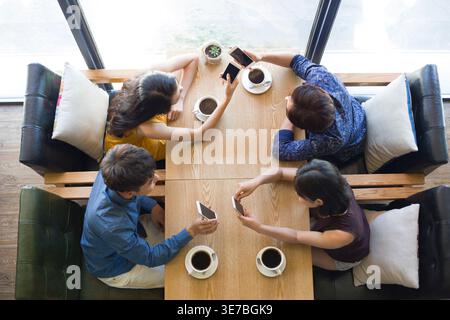 Chinesische Freunde, die Smartphones benutzen, während sie am Tisch im Café Kaffee trinken Stockfoto