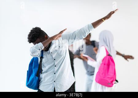 Schwarzer männlicher Student, der mit Rucksack in der Nähe verschiedener Klassenkameraden vor weißem Hintergrund im Studio steht Stockfoto