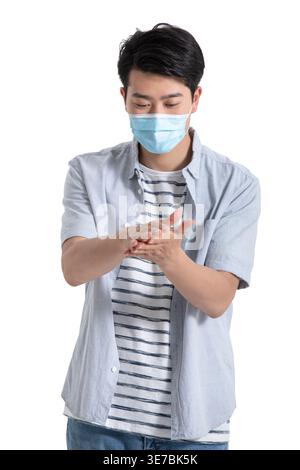 Chinesischer Mann, der eine Gesichtsmaske mit Handdesinfektionsmittel trägt, der vor weißem Hintergrund im Studio steht Stockfoto