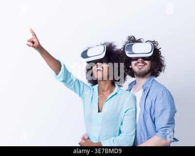 Lächelnde schwarze Frau mit lockigem Afro und kaukasischem Freund, der VR-Headsets trägt und virtuelle Realität erlebt, während er gegen ... dicht beieinander steht Stockfoto