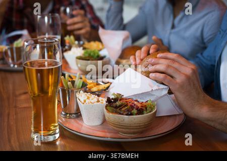 Schwarzer Mann isst Burger mit kaukasischen Freunden, die an einem Tisch in der Bar sitzen Stockfoto