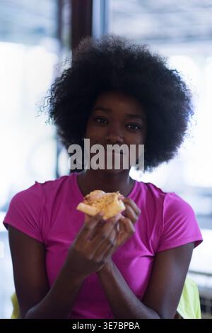 Lächelnde schwarze Frau mit Afro, die Pizza hält, während sie drinnen steht Stockfoto