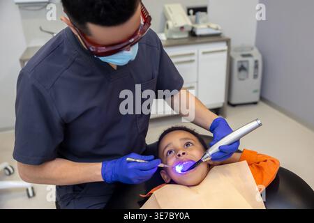 Schwarzer Junge bei zahnärztlicher Behandlung mit kaukasischem Zahnarzt in der Klinik Stockfoto