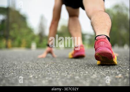 Asiatischer Mann in Sportbekleidung, der sich mit Händen auf dem Boden nach vorne lehnt und sich darauf vorbereitet, draußen zu laufen Stockfoto