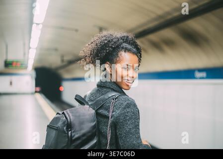 Lächelnde schwarze Frau, die über die Schulter blickt und auf dem U-Bahnhof steht Stockfoto