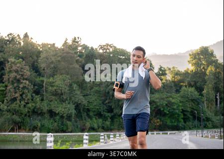 Seriöser asiatischer Mann in Sportbekleidung, der sich beim Laufen im Park den Schweiß ins Gesicht reibt Stockfoto