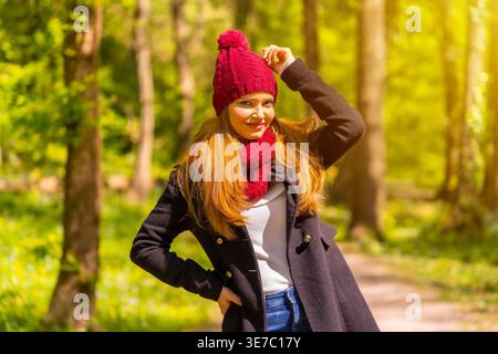 Hispanische Frau in warmer Kleidung und Schal, Arm und Hand auf Taille, die tagsüber im Herbstpark steht Stockfoto