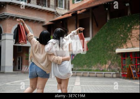 Asiatische Freundinnen halten Einkaufstaschen hoch und stehen tagsüber auf der Straße Stockfoto