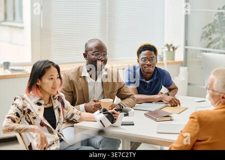Lächelnde Gruppe von Programmierern, die sich am Schreibtisch im Büro treffen Stockfoto