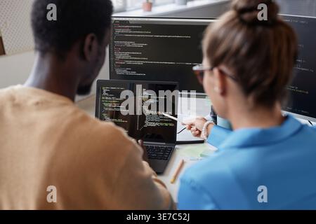 Schwarze männliche und kaukasische Programmiererinnen diskutieren Computercodes auf Laptop, sitzen zusammen am Tisch im Büro Stockfoto