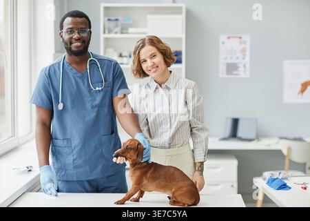 Schwarzer Tierarztmann, der tagsüber neben der kaukasischen Frau in der Nähe des Tisches mit Hund in der Klinik steht Stockfoto