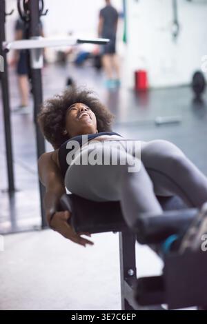 Fröhliche schwarze Frau mit Afro-Kleidung, die auf der bauchbank im Fitnessstudio Sit-ups-Übungen macht Stockfoto