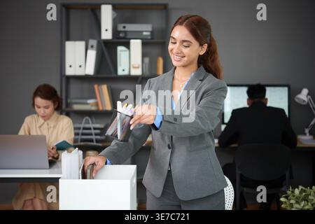 Asiatische Geschäftsfrau, die persönliche Sachen aus der Kiste nimmt und am Schreibtisch im Büro steht Stockfoto