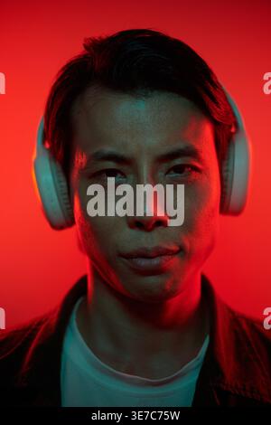 Asiatischer Mann mit Kopfhörern, die vor rotem Neonhintergrund stehen Stockfoto