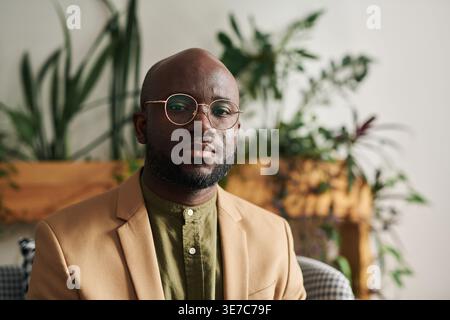 Schwarzer Glatzkopf, männlicher Psychologe, der eine Brille trägt und im Büro auf der Couch sitzt Stockfoto