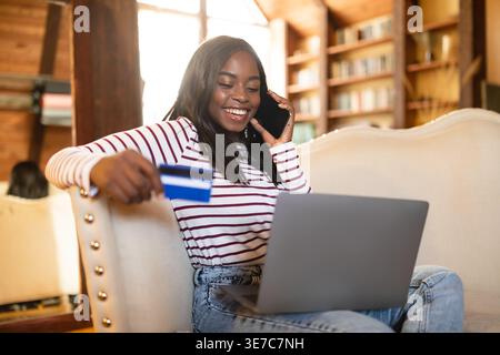 Schwarze Teenager-Frau mit Kreditkarte, die einen Anruf mit Laptop auf der Couch zu Hause hat Stockfoto