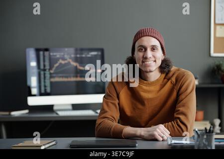 Gemischter männlicher IT-Mitarbeiter mit Händen am Tisch, der vor dem Computer sitzt und Finanzgrafik-Daten auf dem Bildschirm im Büro anzeigt Stockfoto
