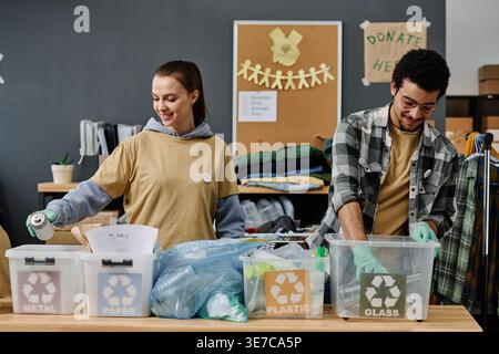 Männliche und kaukasische Freiwillige mit Handschuhen, die Müll auf dem Tisch im Büro sortieren Stockfoto