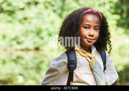 Die Kundschafterin aus gemischtem Rennen trägt einen Rucksack und steht am sonnigen Tag im Wald Stockfoto