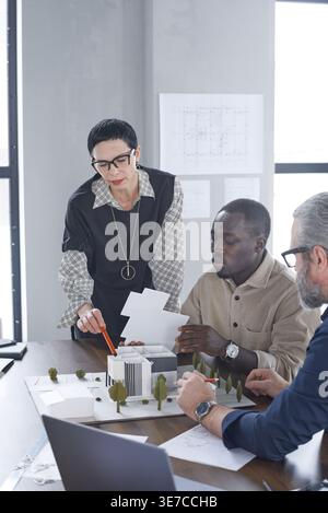 Gruppe von Architekten diskutiert Miniaturmodellbau, während sie während der Besprechung im Büro zusammen am Tisch sitzen Stockfoto