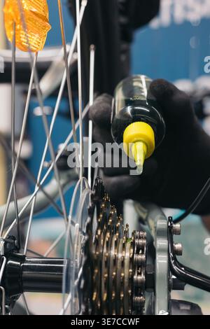 Hände eines hispanischen Mechanikers mit Handschuhen, die beim Hocken in der Werkstatt Öl auf Fahrradketten auftragen Stockfoto