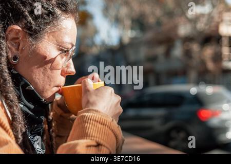 Hispanische Frau mit Dreadlocks, die eine Brille trägt und tagsüber Kaffee trinkt, während sie am Tisch im Café im Freien sitzt Stockfoto