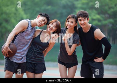 Fröhliche chinesische Freunde stehen tagsüber auf dem Basketballfeld nahe beieinander Stockfoto