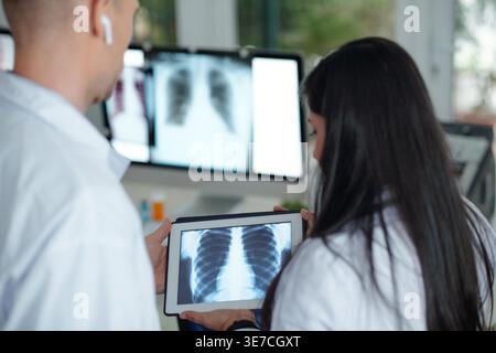 Indische weibliche und kaukasische Ärztinnen diskutieren Thoraxröntgenaufnahme des Patienten auf Tablette im Krankenhaus Stockfoto
