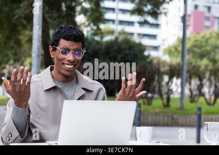 Verwirrter hispanischer Mann mit Brille, der auf den Laptop-Bildschirm blickt und tagsüber am Tisch im Café sitzt Stockfoto