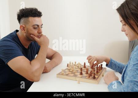 Gemischte Rasse und kaukasisches Paar spielen zu Hause Schach auf dem Tisch Stockfoto