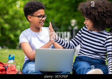 Schwarze Teenager geben sich gegenseitig High Fives, während sie im Park auf Gras sitzen Stockfoto