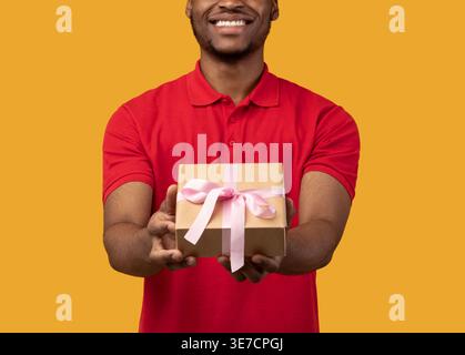 Schwarzer Mann mit Mütze, der Geschenk hält, steht vor gelbem Hintergrund im Studio Stockfoto