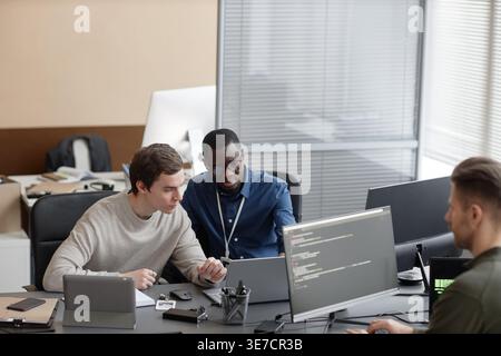Verschiedene männliche IT-Spezialisten arbeiten zusammen und sitzen am Schreibtisch mit Laptop und Computern im Büro Stockfoto