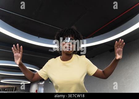 Schwarze Frau mit Afro, die eine futuristische, intelligente Brille trägt, während sie in einem Gebäude steht Stockfoto