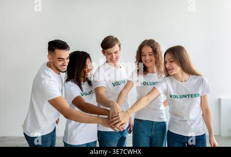 Eine lächelnde Gruppe Freiwilliger stapelt sich die Hände zusammen, während sie im Studio gegen die weiße Wand stehen Stockfoto