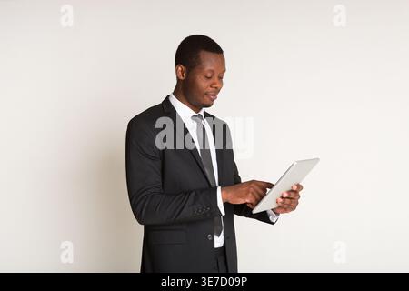 Schwarzer Geschäftsmann, der ein Tablet benutzt, während er im Studio vor weißem Hintergrund steht Stockfoto