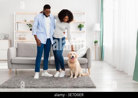Lächelnde Schwarze, die mit ihrem Hund spielen, während sie zu Hause im Wohnzimmer stehen Stockfoto