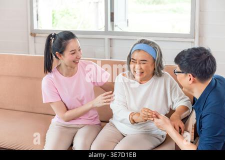 Ältere asiatische Frau lacht, während sie mit ihrem Sohn und ihrer Tochter im Wohnzimmer zu Hause auf dem Sofa sitzt Stockfoto