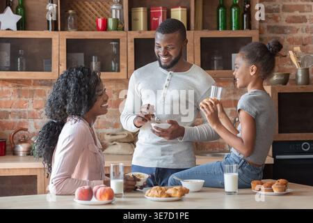 Fröhliche schwarze Familie, die sich beim Frühstück in der Küche zu Hause unterhält Stockfoto