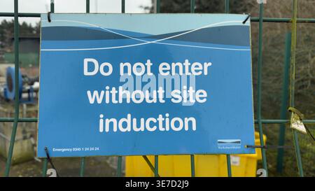 Blaues Schild mit weißem Text mit der Aufschrift „Do not entry without Site Induction“ auf grünem Metallzaun. Stockfoto