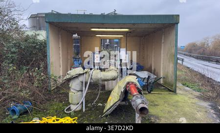 Gefährdete Pumpenstation mit großen Rohrleitungen, Maschinen und überwachsenen Büschen unter einem offenen Schutzdach. Stockfoto