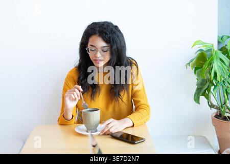 Hispanische Frau mit Brille und Kaffee, während sie am Tisch im Café sitzt Stockfoto