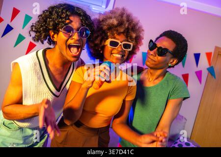 Eine Gruppe von Freunden mit Sonnenbrille, die zu Hause tanzen und Karaoke singen Stockfoto